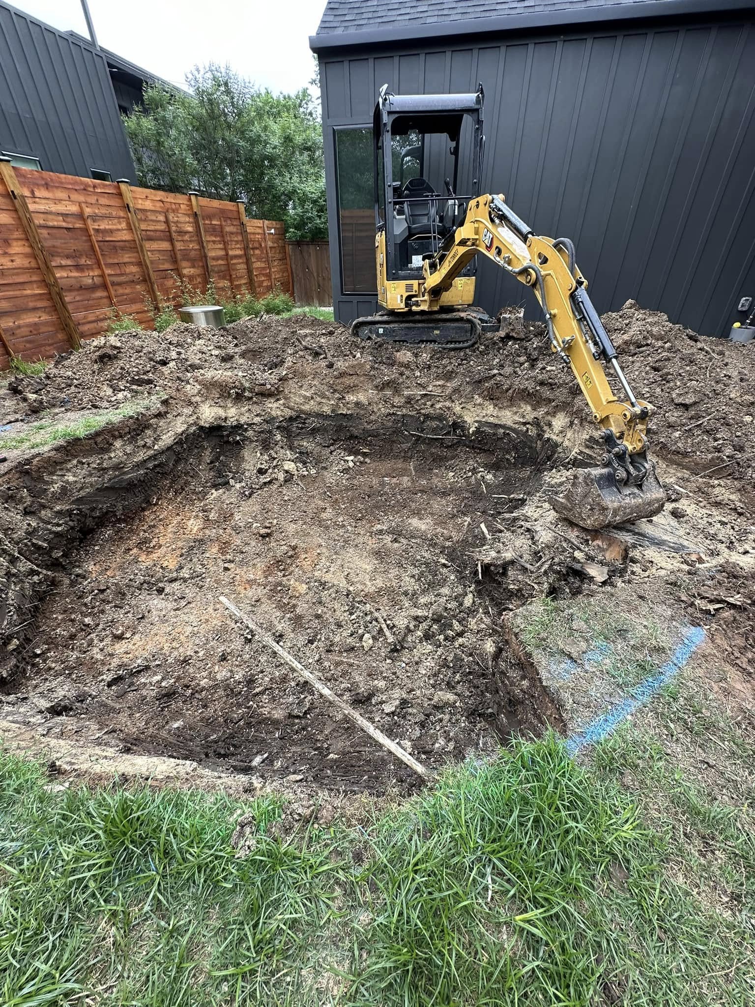CAT mini excavator digging deep circular pit in backyard